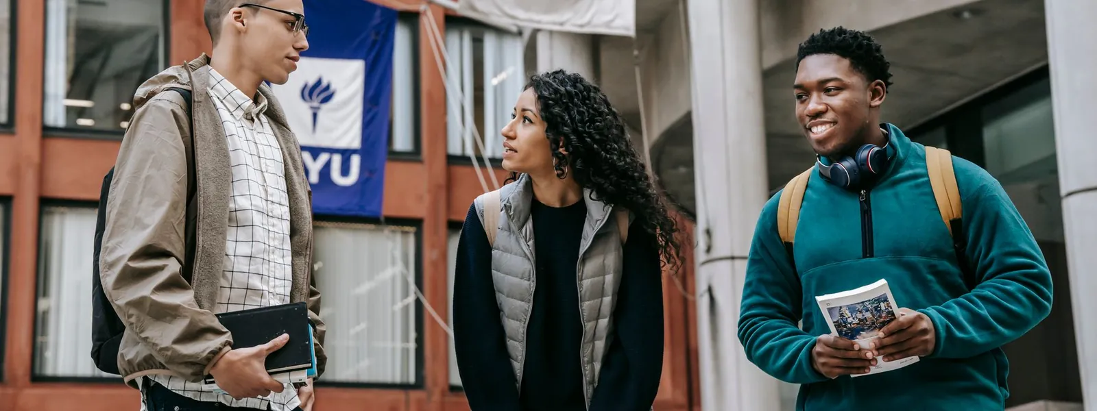Groupe d'étudiants internationaux échangeant des documents près d'un bâtiment universitaire