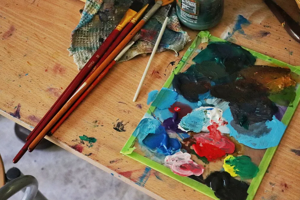 Une palette de peinture colorée et des pinceaux posés sur une table d'artiste