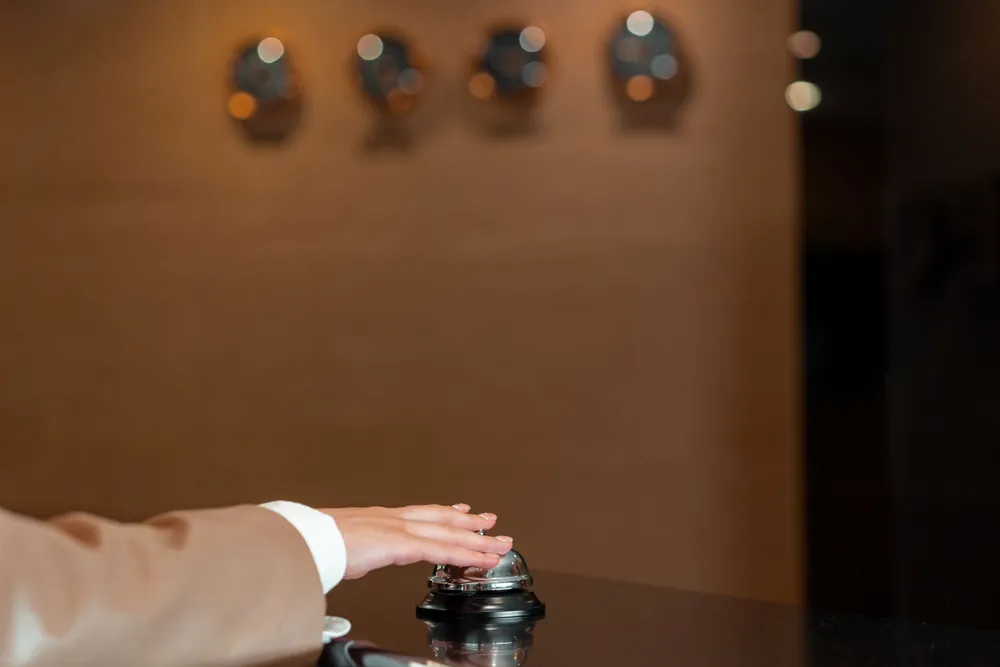 Main appuyant sur une clochette à la réception d'un hôtel