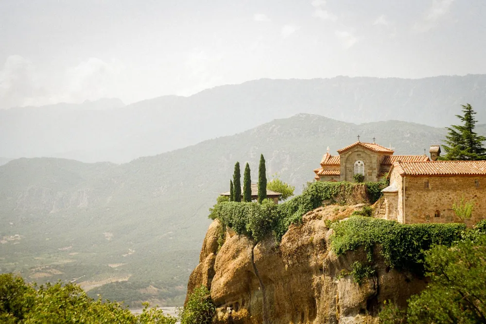 Un monastère perché sur une falaise avec des montagnes en arrière-plan en Grèce