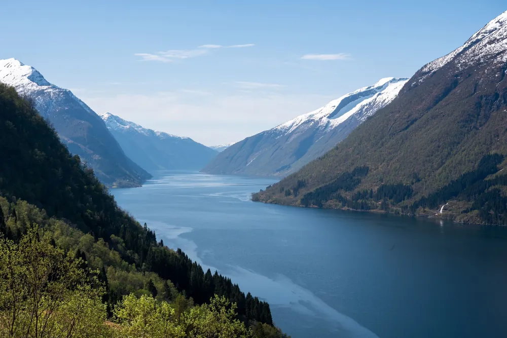 Fjord norvégien encadré de montagnes enneigées et de forêts verdoyantes