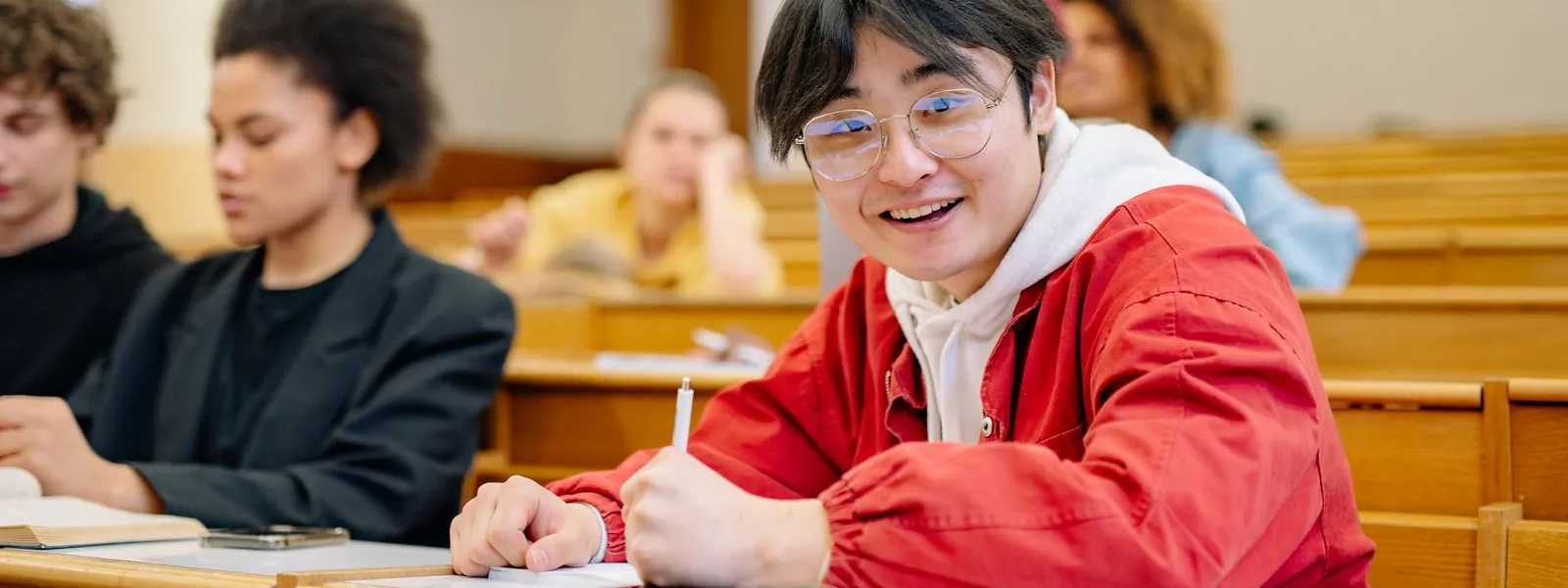 Étudiante souriante prenant des notes dans un amphithéâtre universitaire