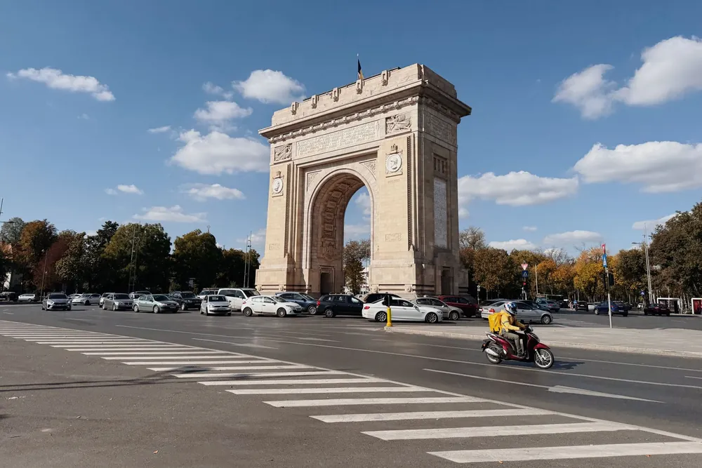 Arc de triomphe de Bucarest se dressant sous un ciel bleu avec circulation environnante
