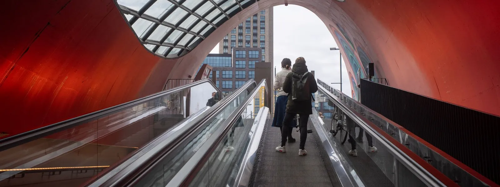 Tunnel moderne d'Eindhoven aux murs rouges et toit de verre où circulent les habitants