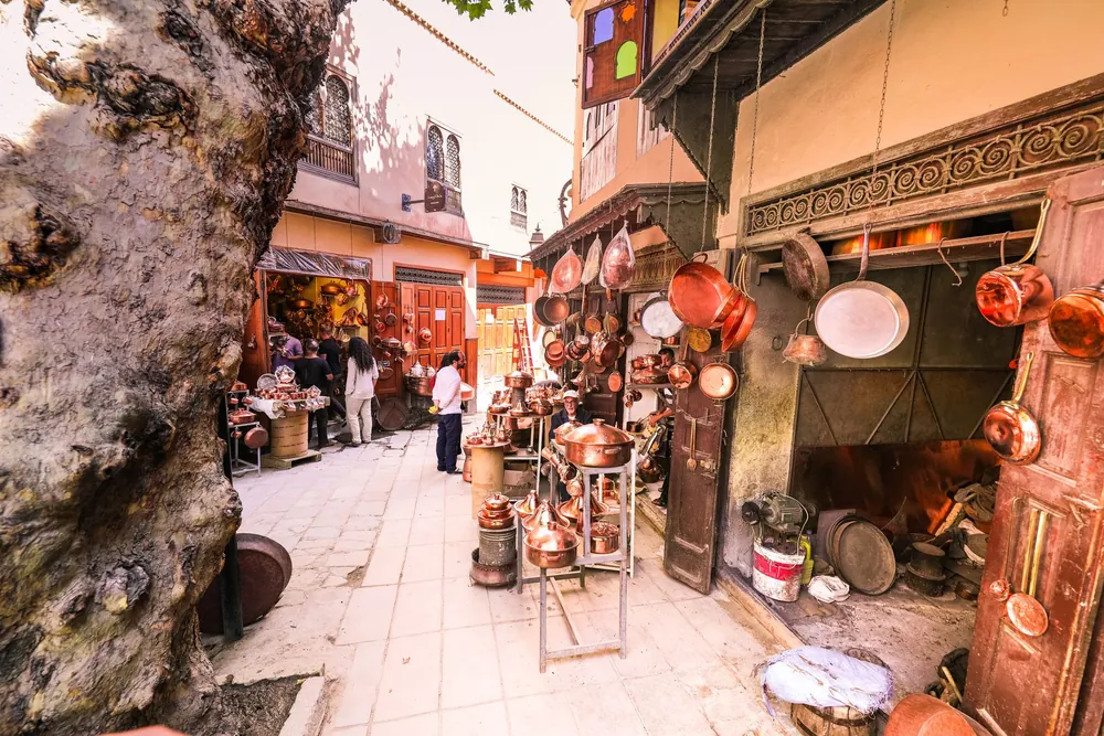 Marché animé de Marrakech avec pots de cuivre suspendus et badauds