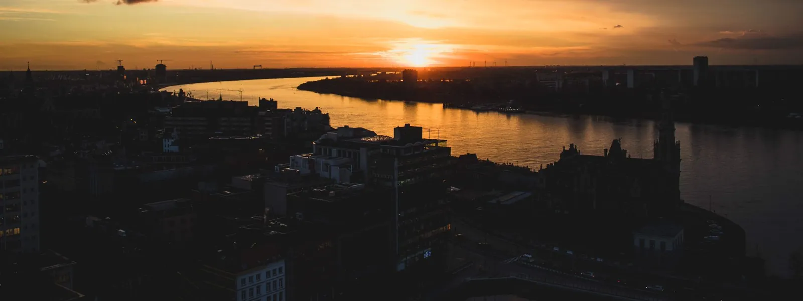Silhouette d'Anvers se dessinant au coucher du soleil au bord du fleuve