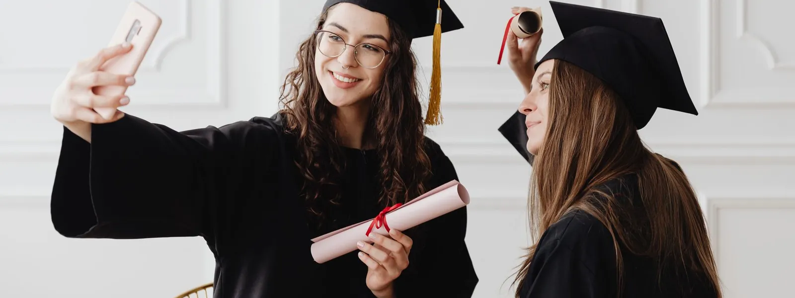 Jeunes diplômées souriantes prenant un selfie en tenue de remise de diplôme